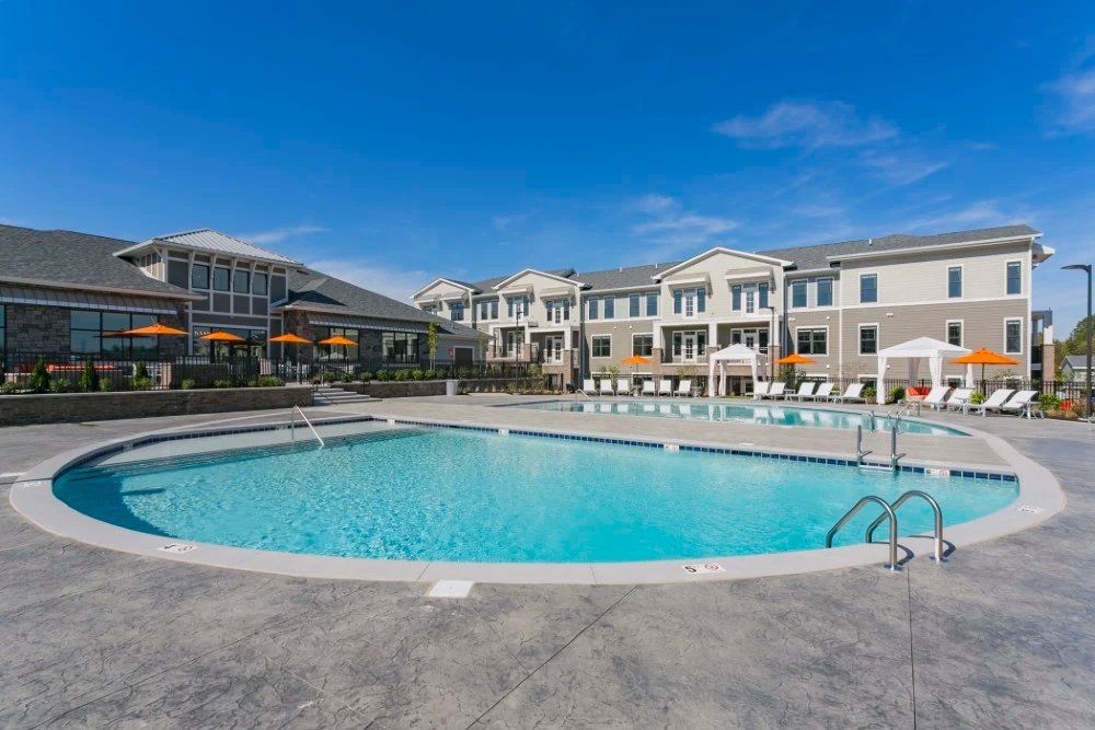 Outdoor apartment pool with blue water, lounge chairs, and modern buildings under a clear sky at Haven on Tucker Apartments in Louisville, KY.
