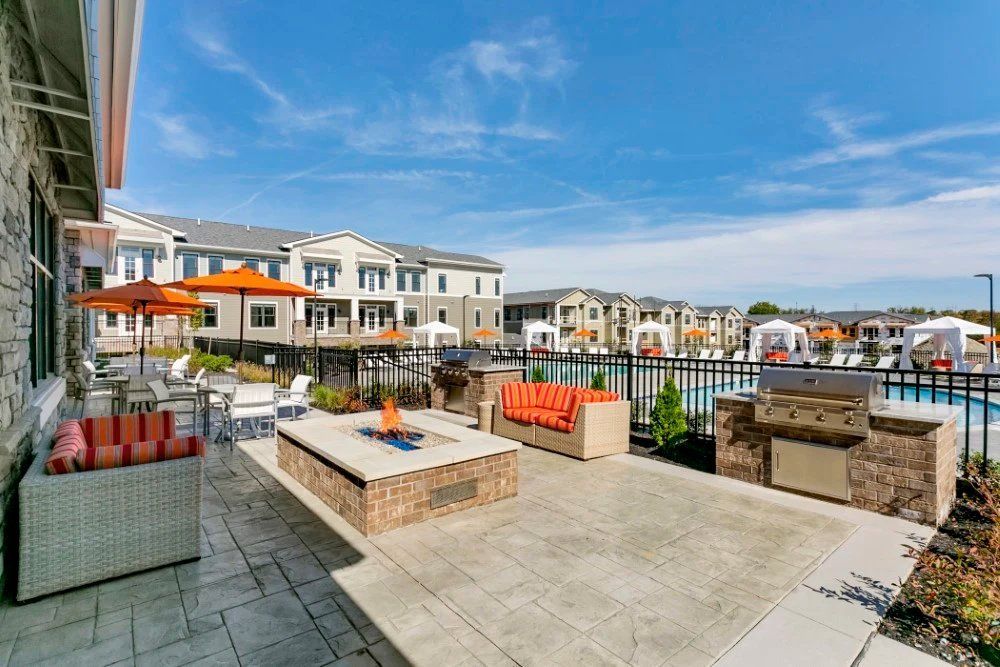 Patio with fire pit and orange umbrellas overlooking modern townhomes under a blue sky at Haven on Tucker Apartments in Louisville, KY.