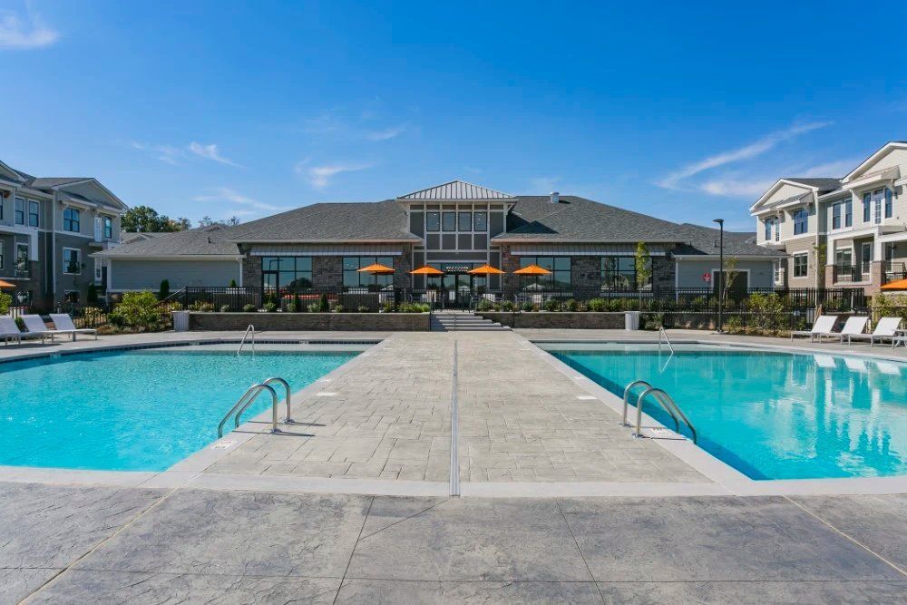 Modern apartment pool courtyard with two blue swimming pools and lounge chairs under a sunny sky at Haven on Tucker Apartments in Louisville, KY.