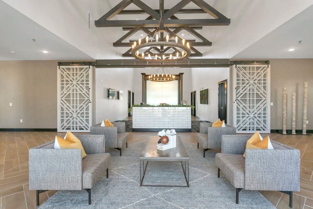 Modern hotel lobby with gray armchairs, glass coffee table, chandelier, and decorative wall panels at Haven on Tucker Apartments in Louisville, KY.