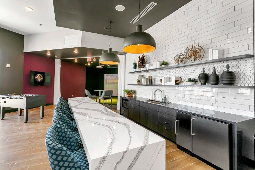 Modern kitchen with white tile backsplash, black cabinets, marble island, and hanging pendant lights at Haven on Tucker Apartments in Louisville, KY.
