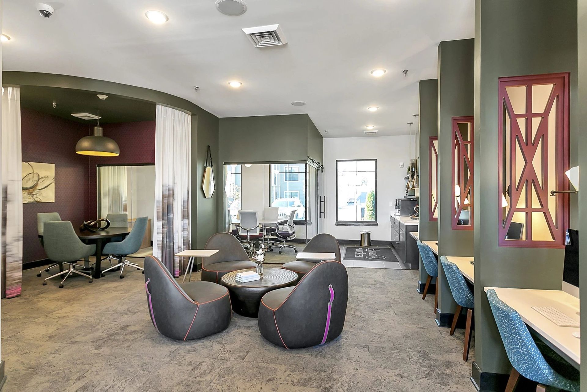 Modern lounge with rounded chairs, gray carpet, and lounge seating by large windows at Haven on Tucker Apartments in Louisville, KY.