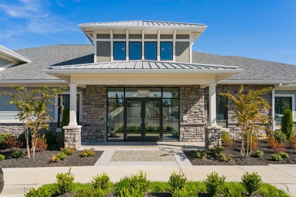 Modern building entrance with stone facade, glass doors, and a landscaped front walkway at Haven on Tucker Apartments in Louisville, KY.