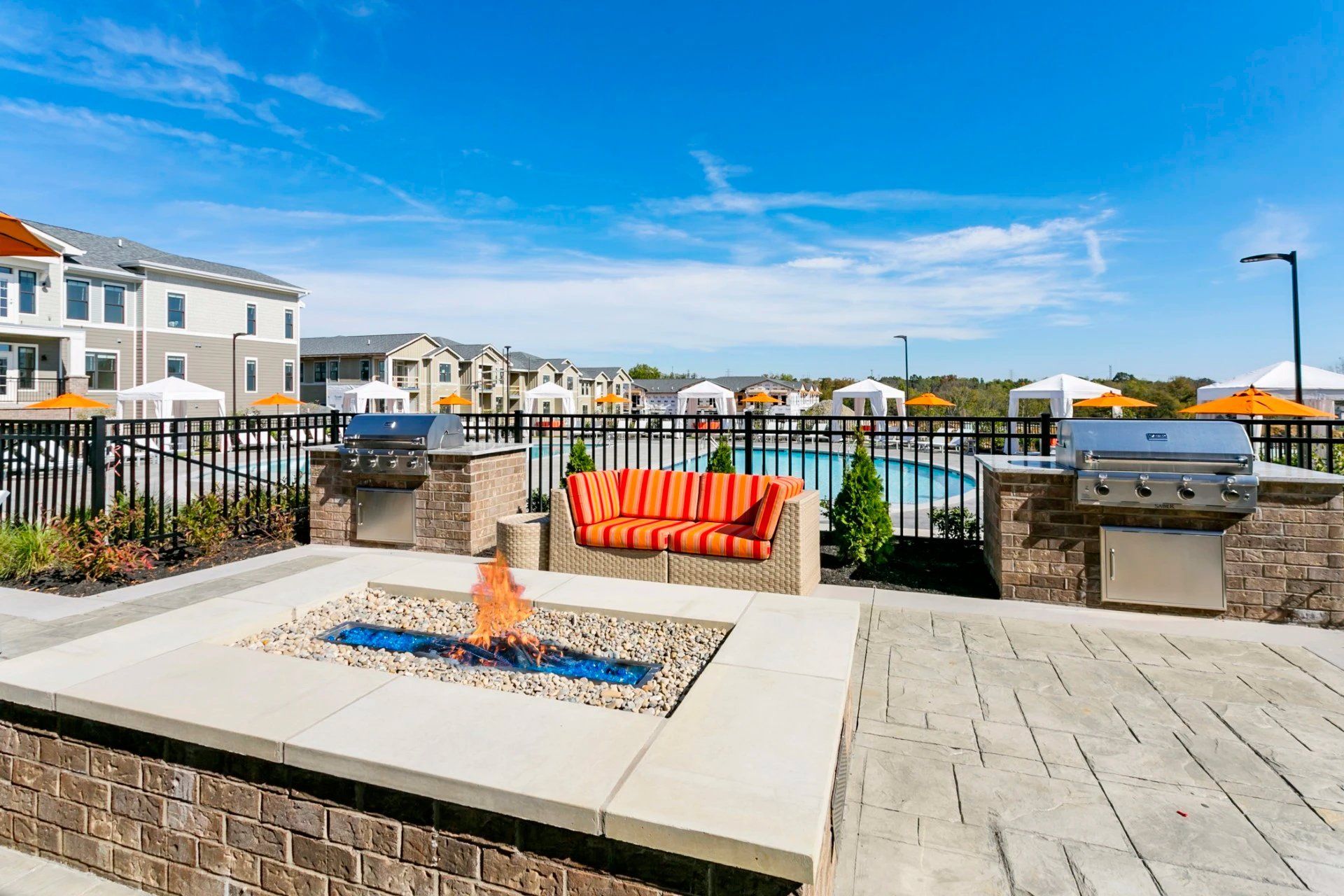 Patio seating area with orange cushions, fire pit, and grill beside waterfront homes and canal views at Haven on Tucker Apartments in Louisville, KY.