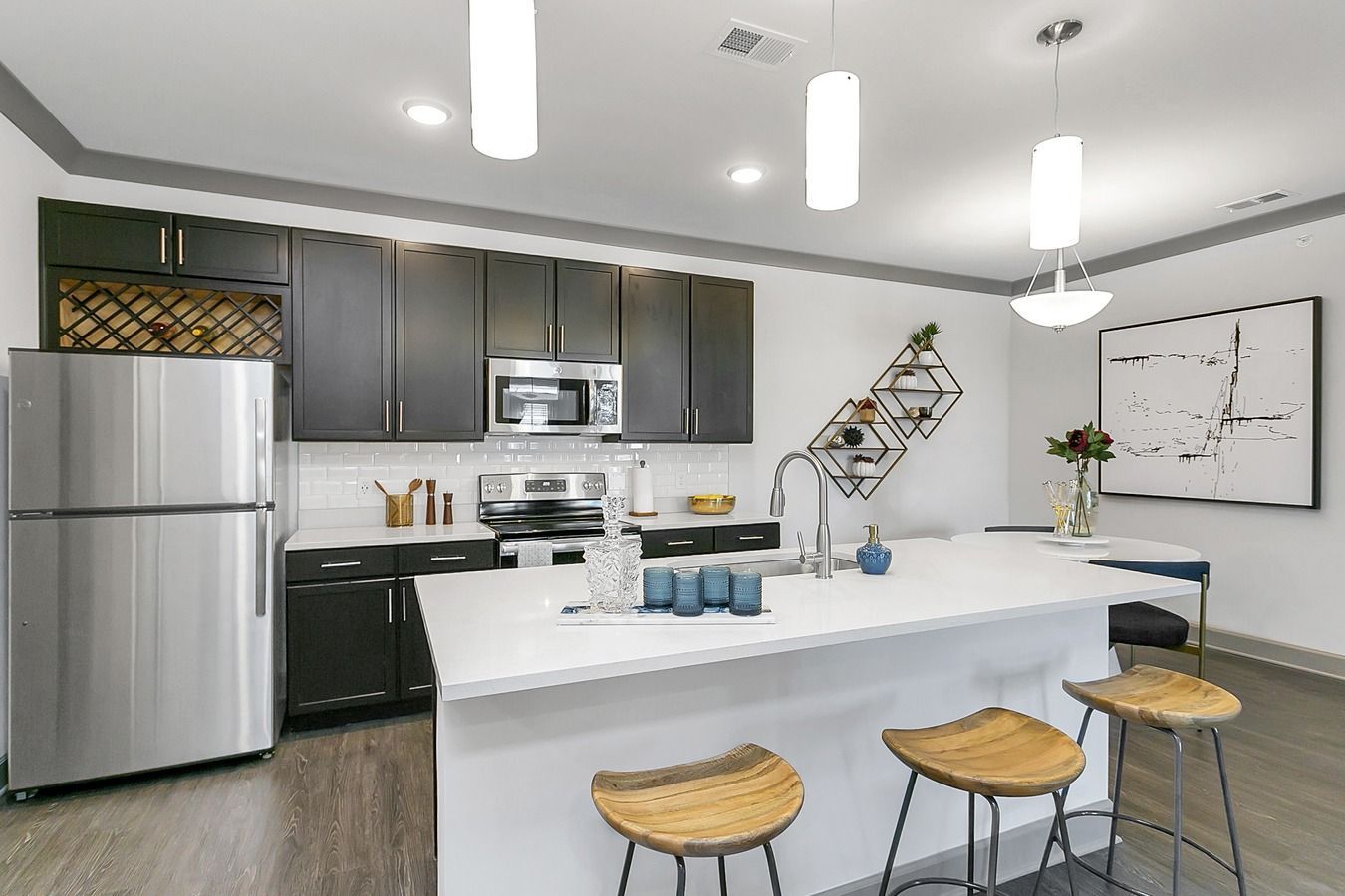 Modern white kitchen with stainless appliances, island seating, pendant lights, and dark gray cabinets at Haven on Tucker Apartments in Louisville, KY