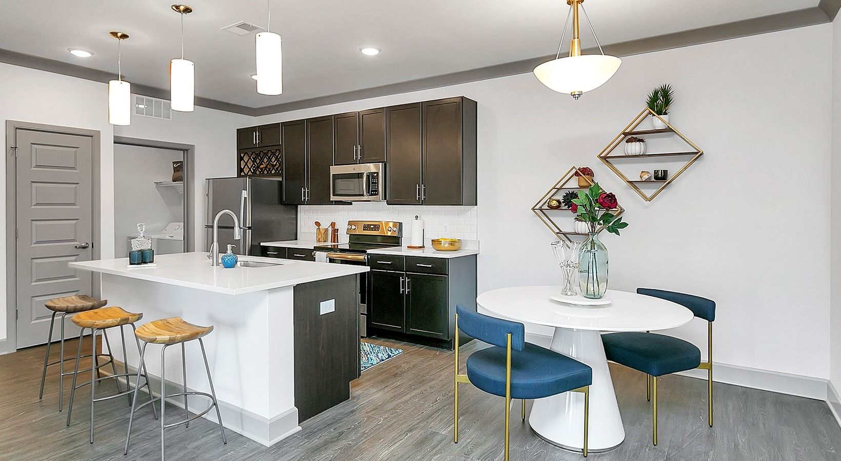 Modern kitchen and dining area with white island, dark cabinets, blue chairs, and pendant lights at Haven on Tucker Apartments in Louisville, KY