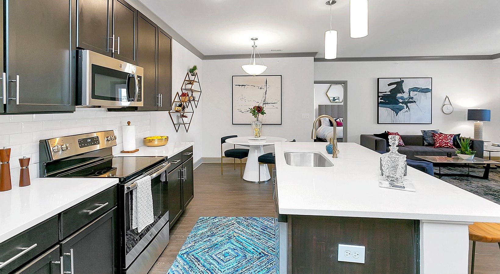 Modern kitchen with white island, stainless appliances, blue rug, and framed wall art at Haven on Tucker Apartments in Louisville, KY