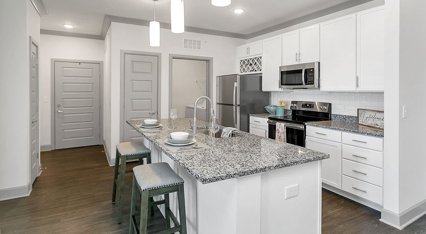 Modern white kitchen with granite island, bar stools, stainless appliances, and pendant lights at Haven on Tucker Apartments in Louisville, KY