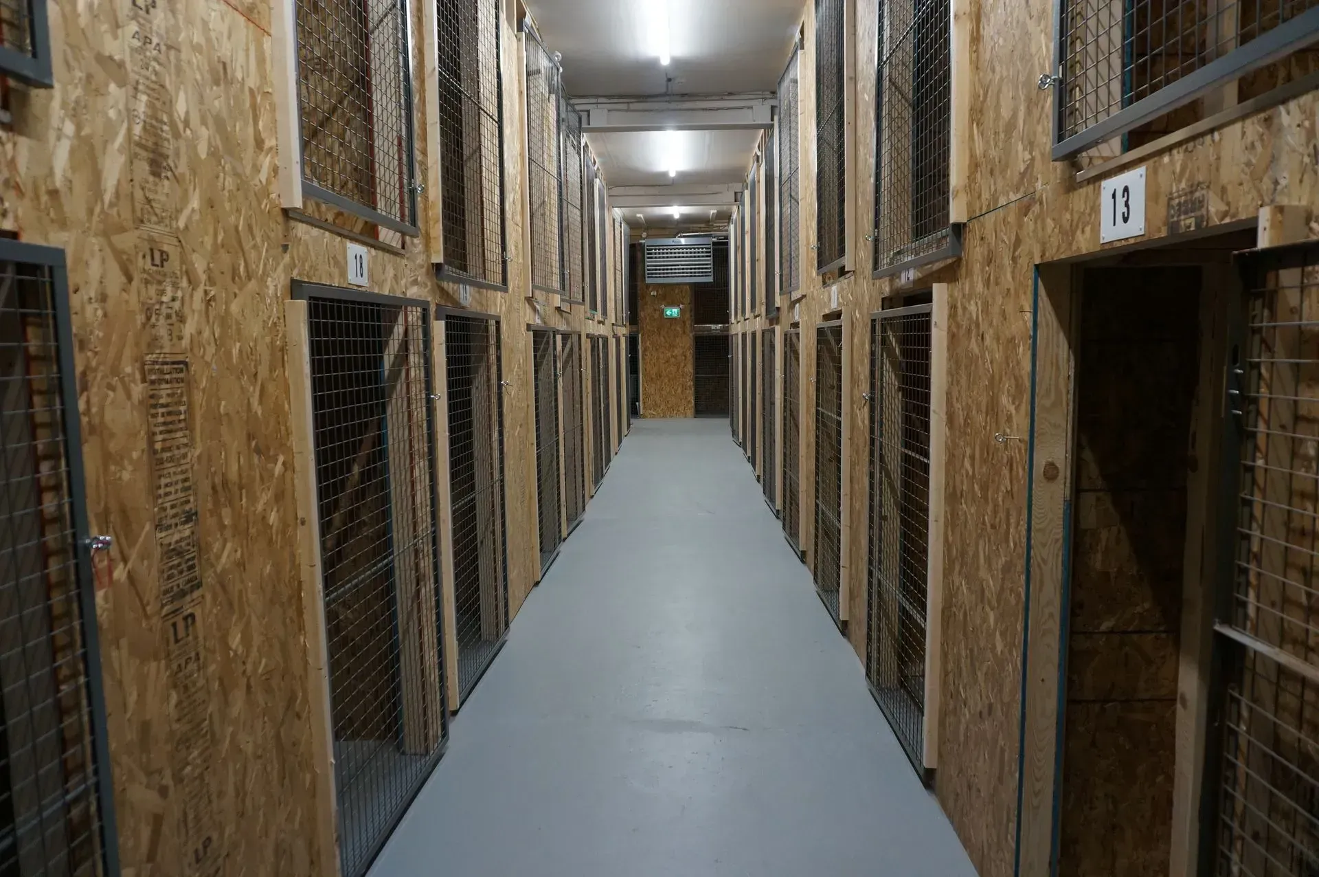 Narrow indoor corridor lined with metal cages or kennels on both sides, with a gray floor.