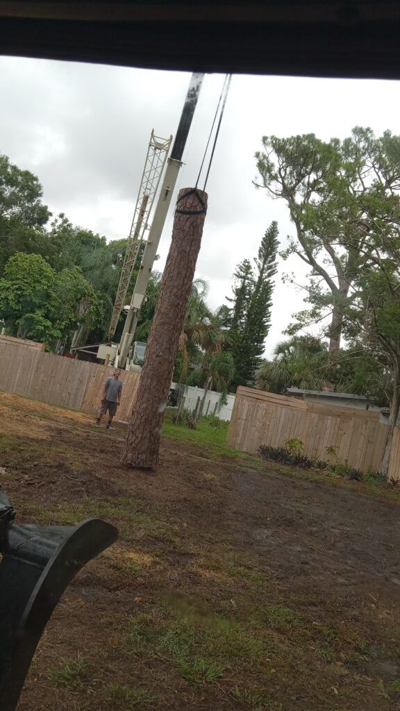 Tall metal poles with a brick column under construction in a muddy yard, with trees and a fence nearby.