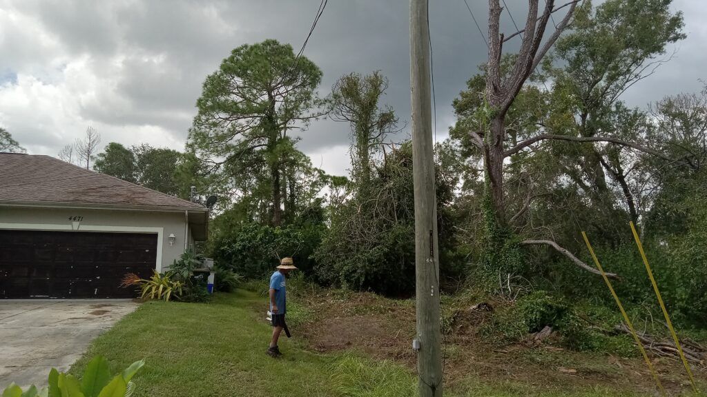 Storm-damaged yard with fallen trees and a person standing near a house garage