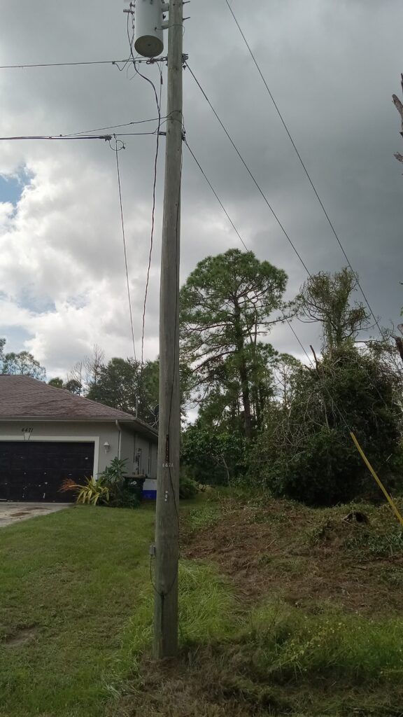 Utility pole beside a grassy yard and house under cloudy skies