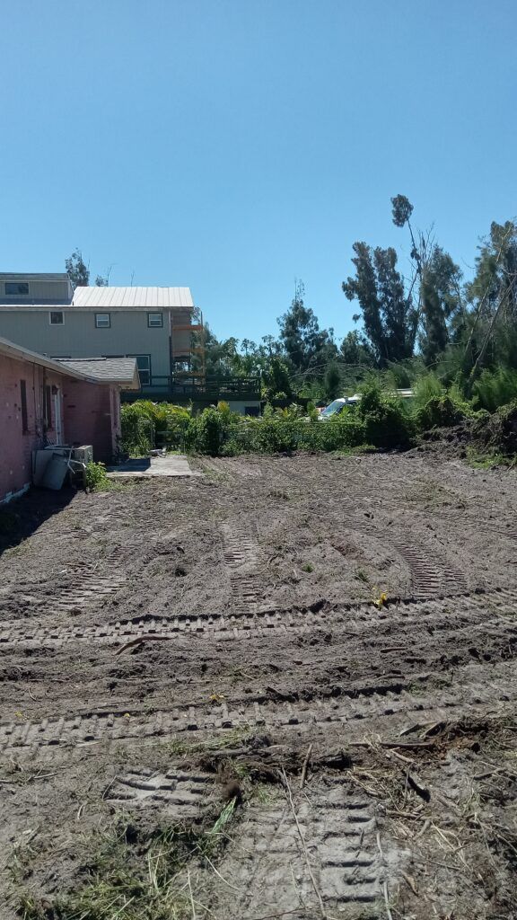 Vacant dirt lot beside a house and trees under a clear blue sky