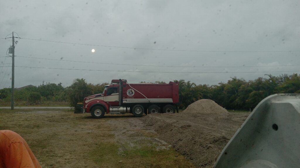 Red dump truck on a gravel lot beside a dirt mound under a cloudy sky