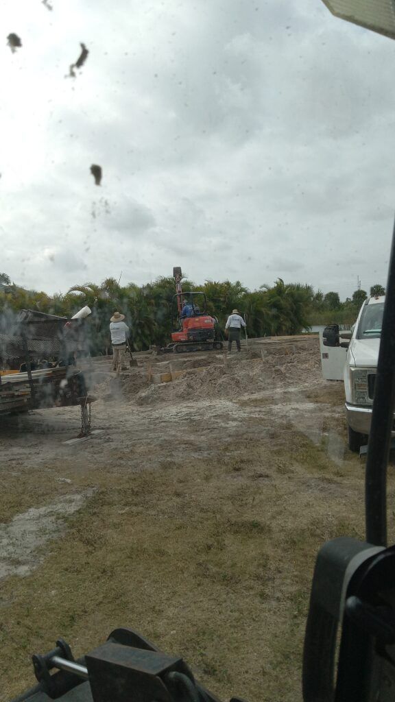 Gravel work site beside a road, with trucks and equipment under a cloudy sky.