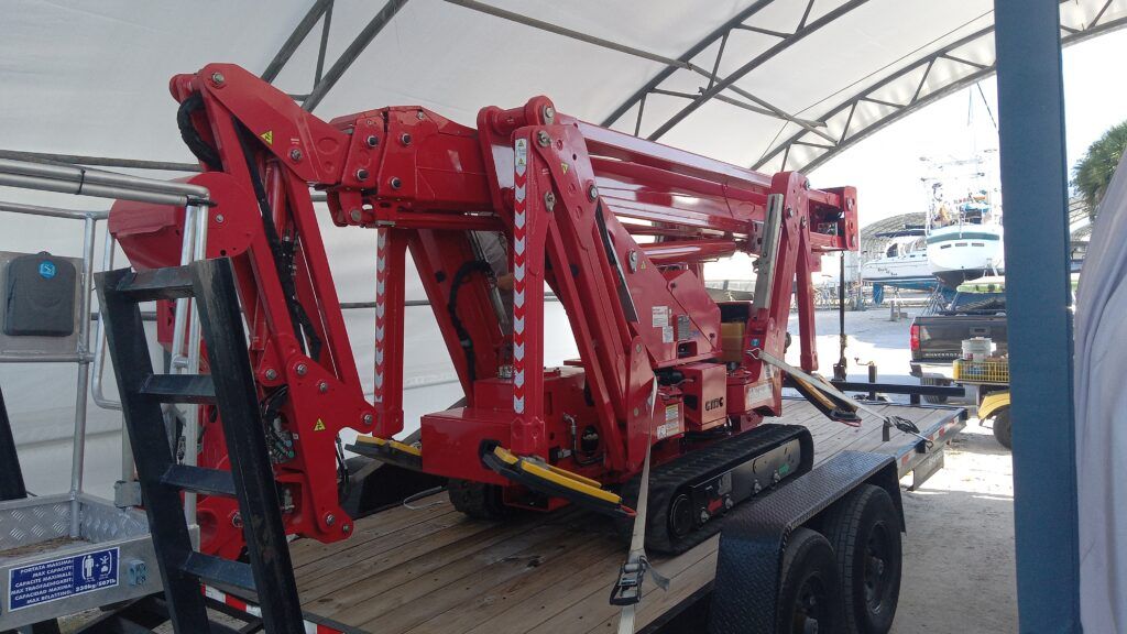 Red hydraulic forklift attachment on a flatbed trailer under a metal canopy, outdoors.