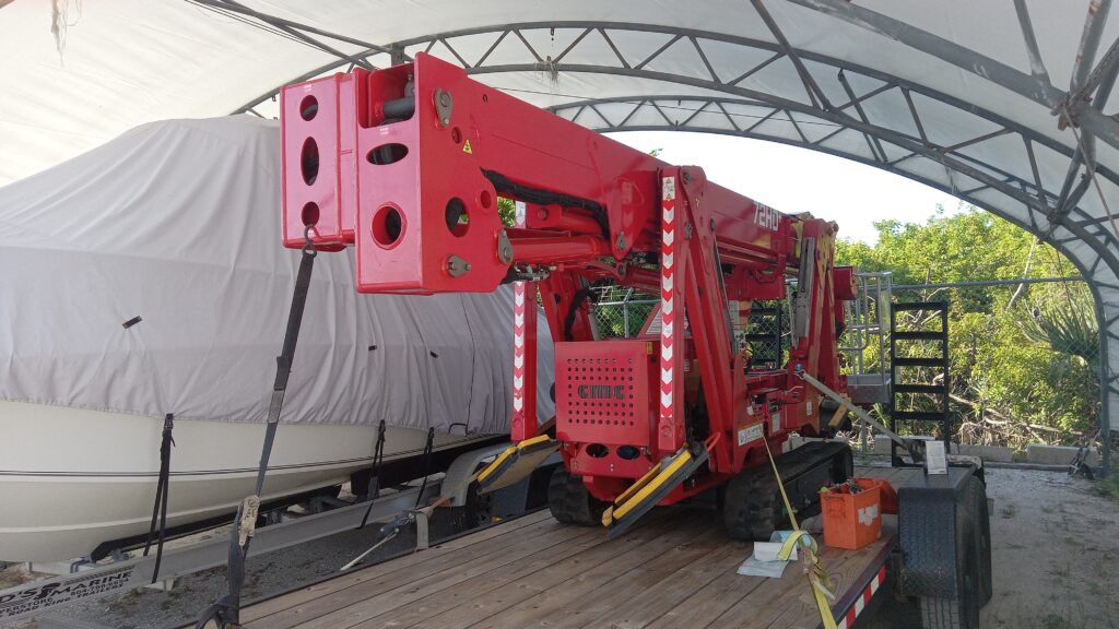Red industrial drilling machine under a canopy beside a covered load on a flatbed trailer