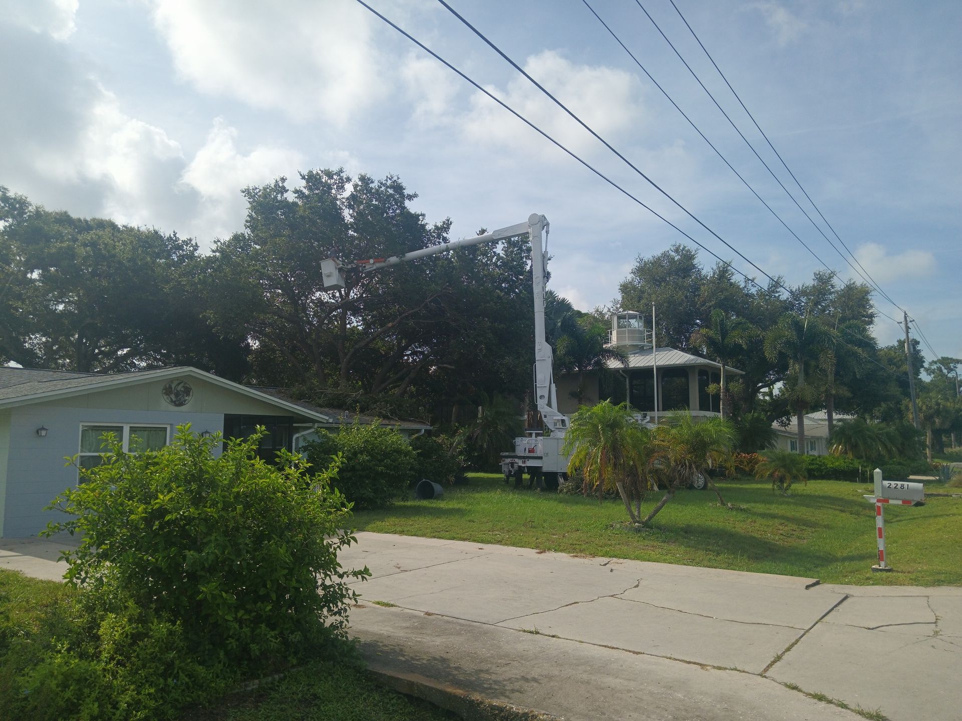 Quiet suburban street with a utility truck working near a house, trees, and overhead power lines.