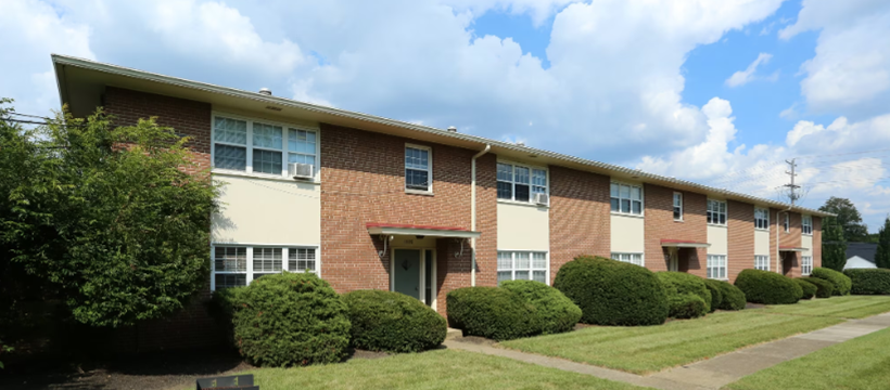 A brick apartment building with a lot of windows and bushes in front of it.