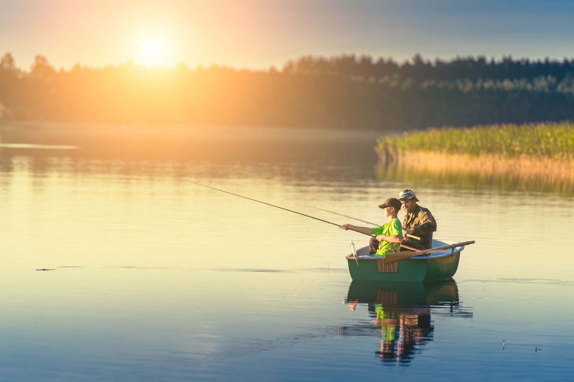 Two people fishing from a small boat on a calm lake at sunrise