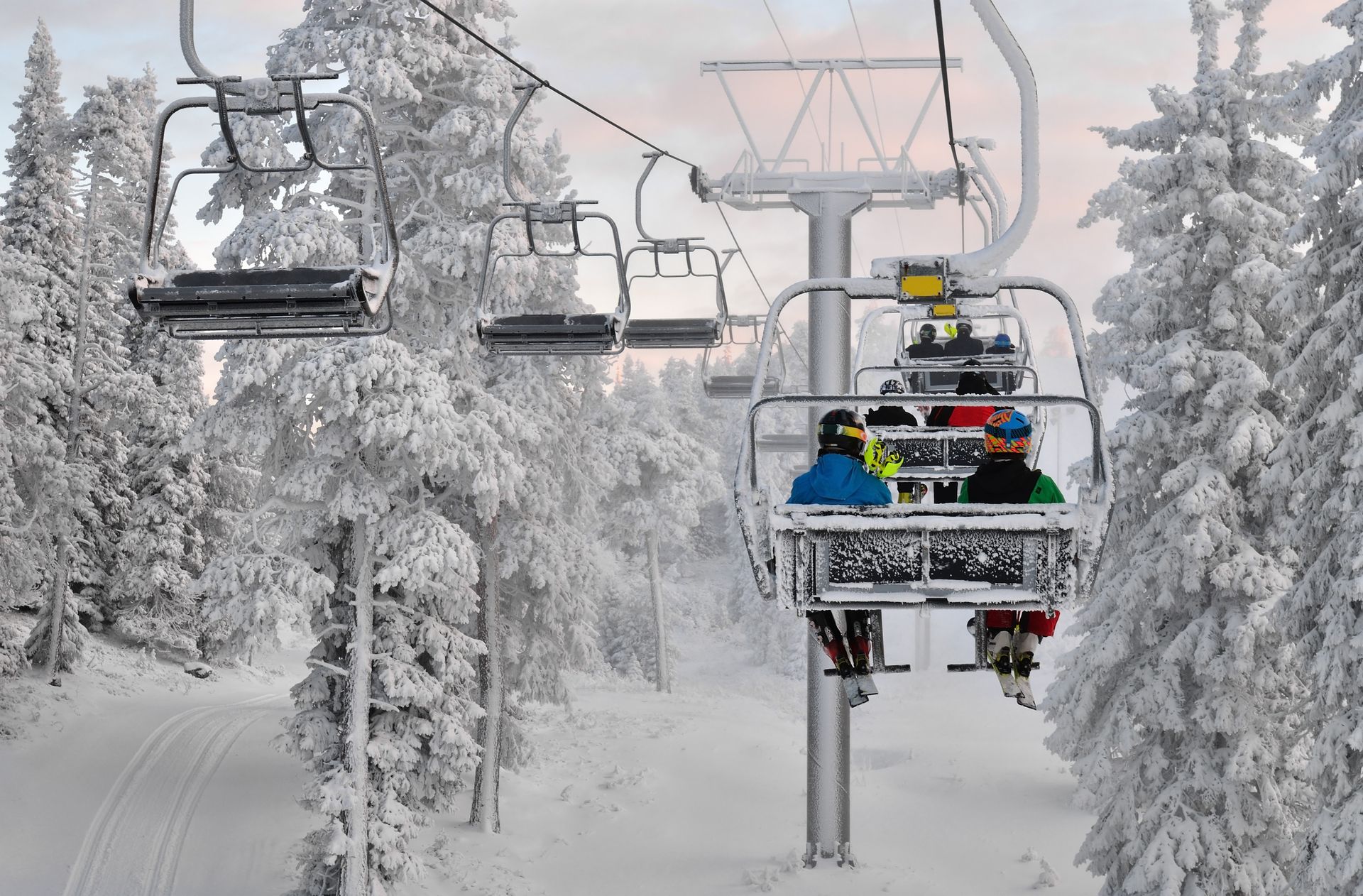 Ski lift chairs carrying bundled skiers through a snowy forest on a winter day