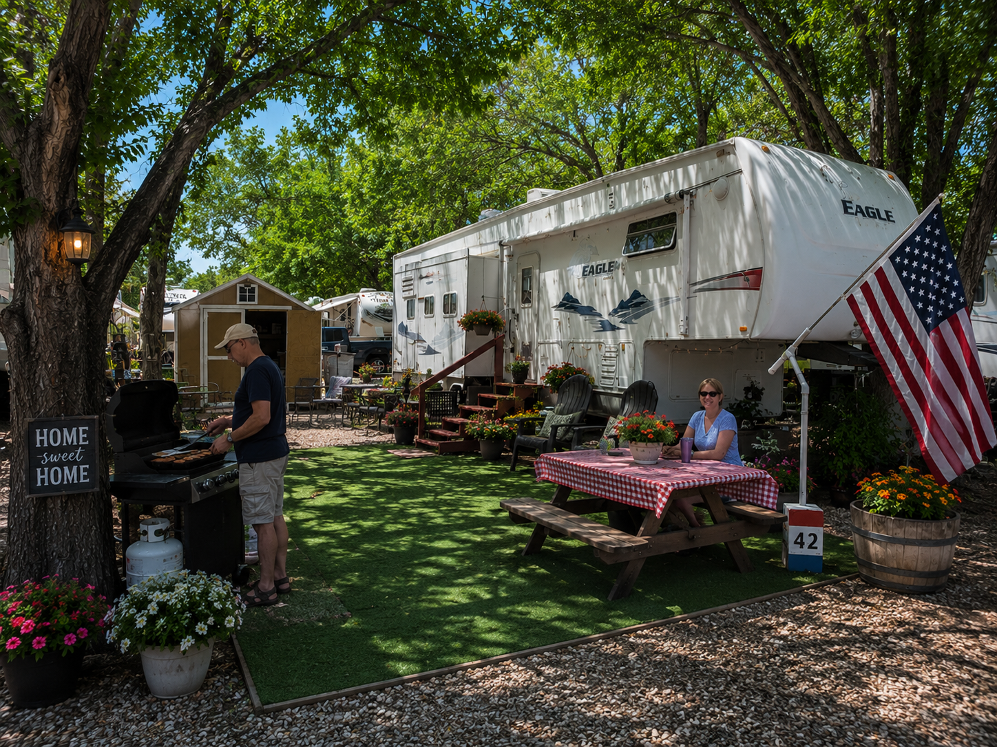 Outdoor yard with white trailer, picnic table, American flag, and people near a tree and plants