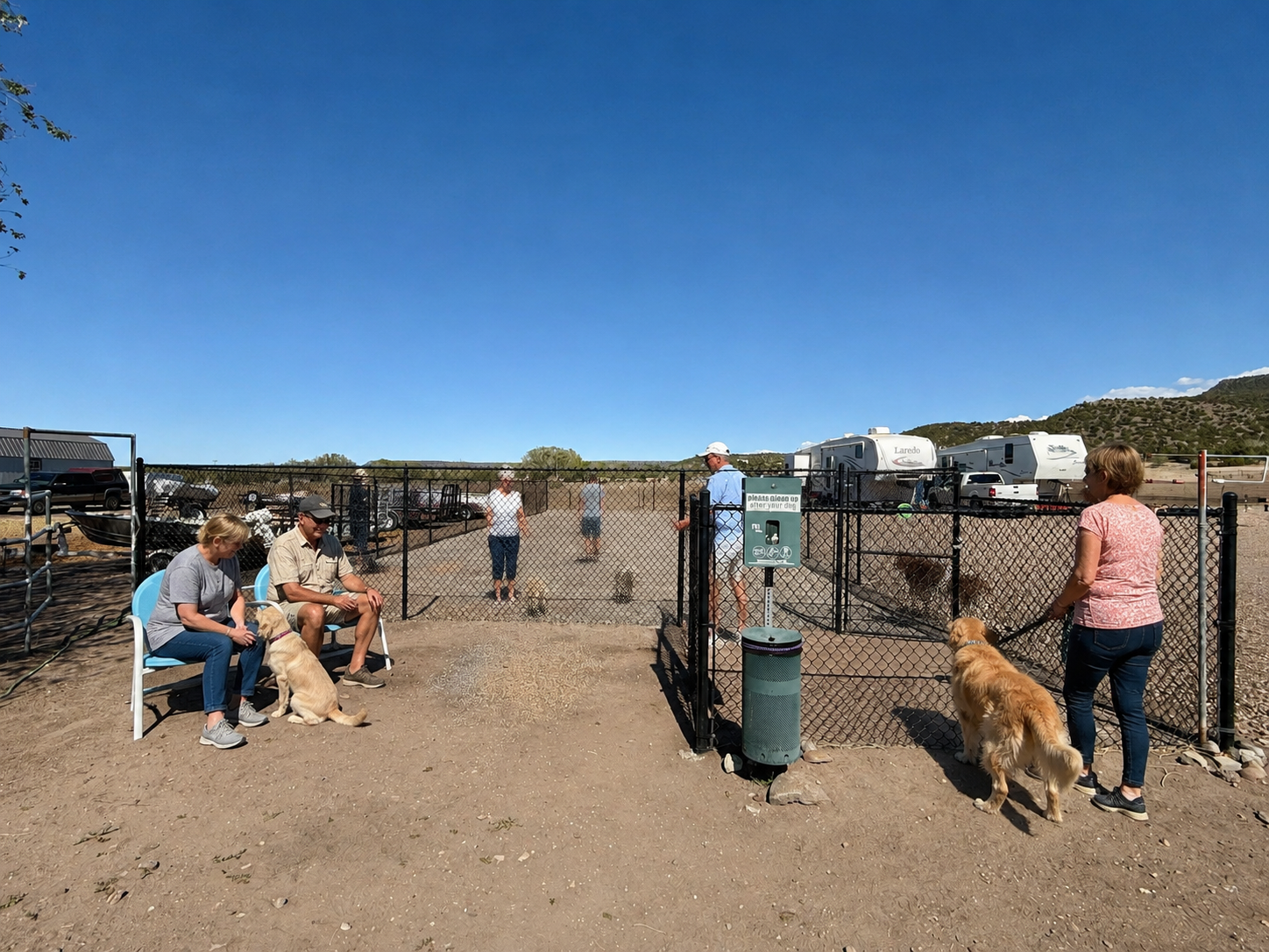 People sitting by a fenced entrance in a dusty desert area, with a dog on leash and RVs in the background