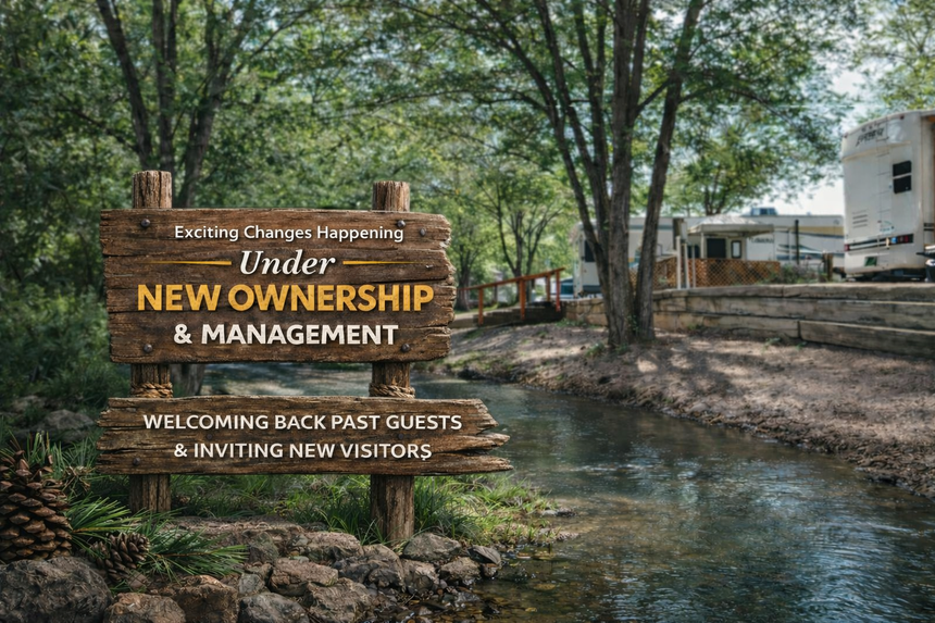 Wooden sign by a creek reads “Under New Ownership & Management” and “Welcome Back Past Guests & Inviting New To”