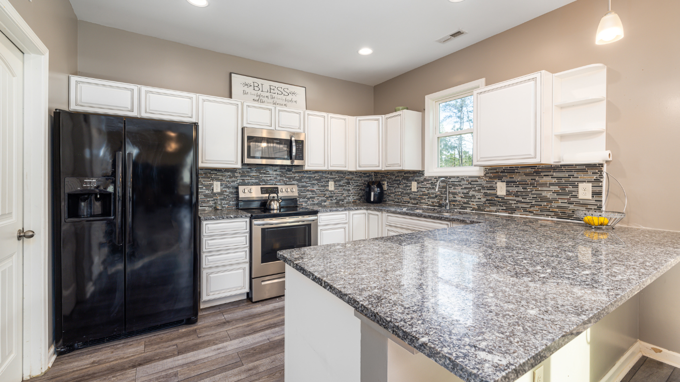 Modern kitchen with white cabinets, black appliances, granite island, and mosaic tile backsplash