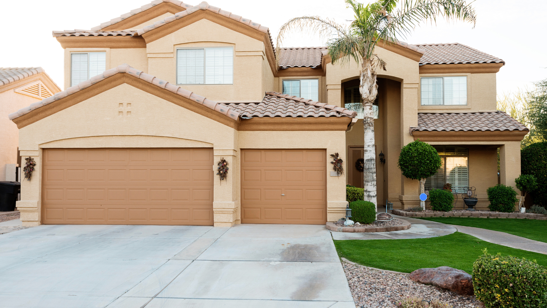 Two-story beige suburban house with a three-car garage, driveway, and front lawn