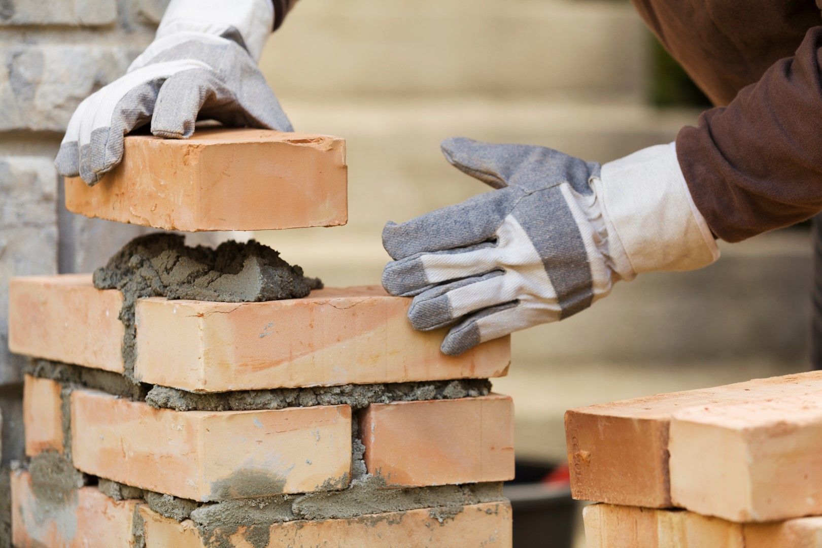 Hands in gloves laying bricks with mortar.
