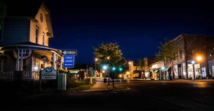 Street view at night with buildings, streetlights, and a dark blue sky.