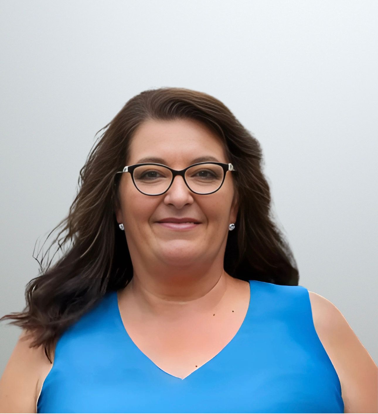 Woman wearing glasses smiles, in blue top, hair flowing, against light gray backdrop.