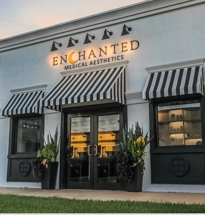 Storefront of Enchanted Medical Aesthetics with striped awnings and illuminated sign at dusk