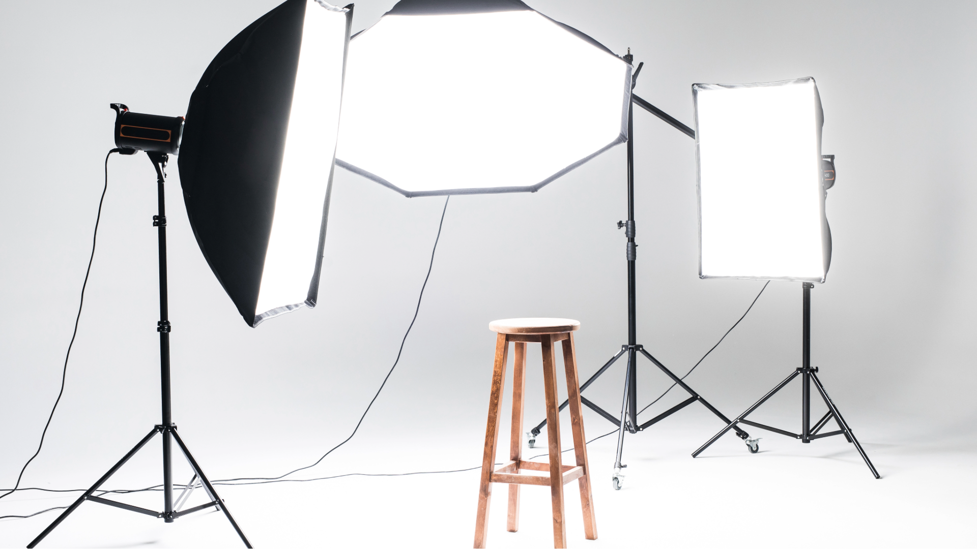 Studio lighting setup with three softbox lights around a wooden stool on a white backdrop