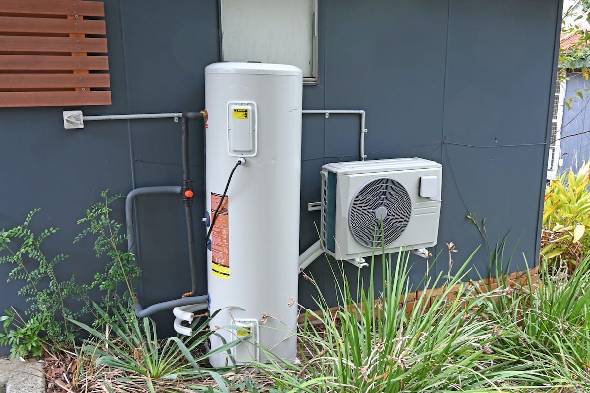 Outdoor Water Heater Unit and Air Conditioner Beside a Grey House Wall — Mark's Plumbing in Lake Haven, NSW