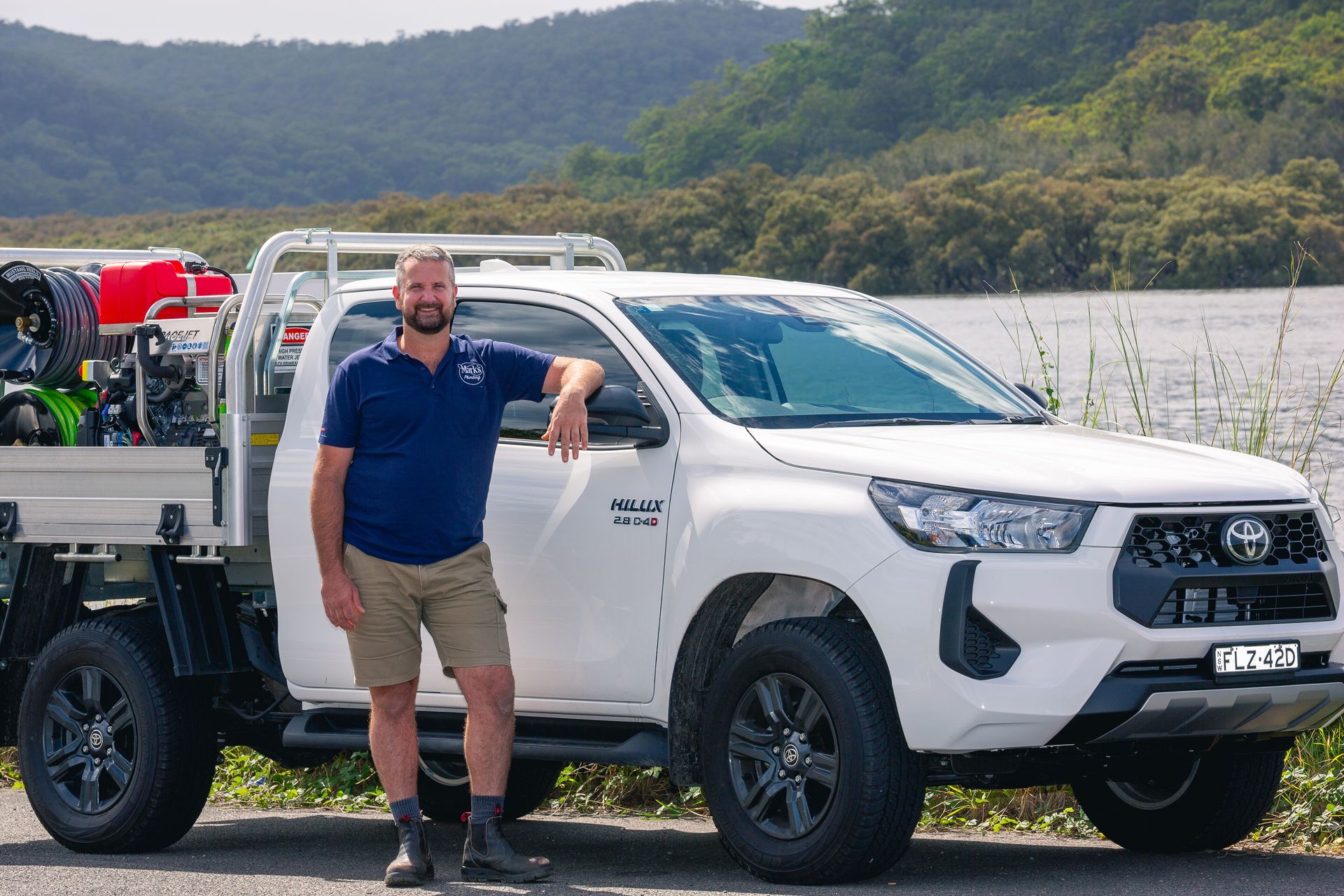 Man Standing Beside a White Pickup Truck by a Lakeside — Mark's Plumbing in Noraville, NSW