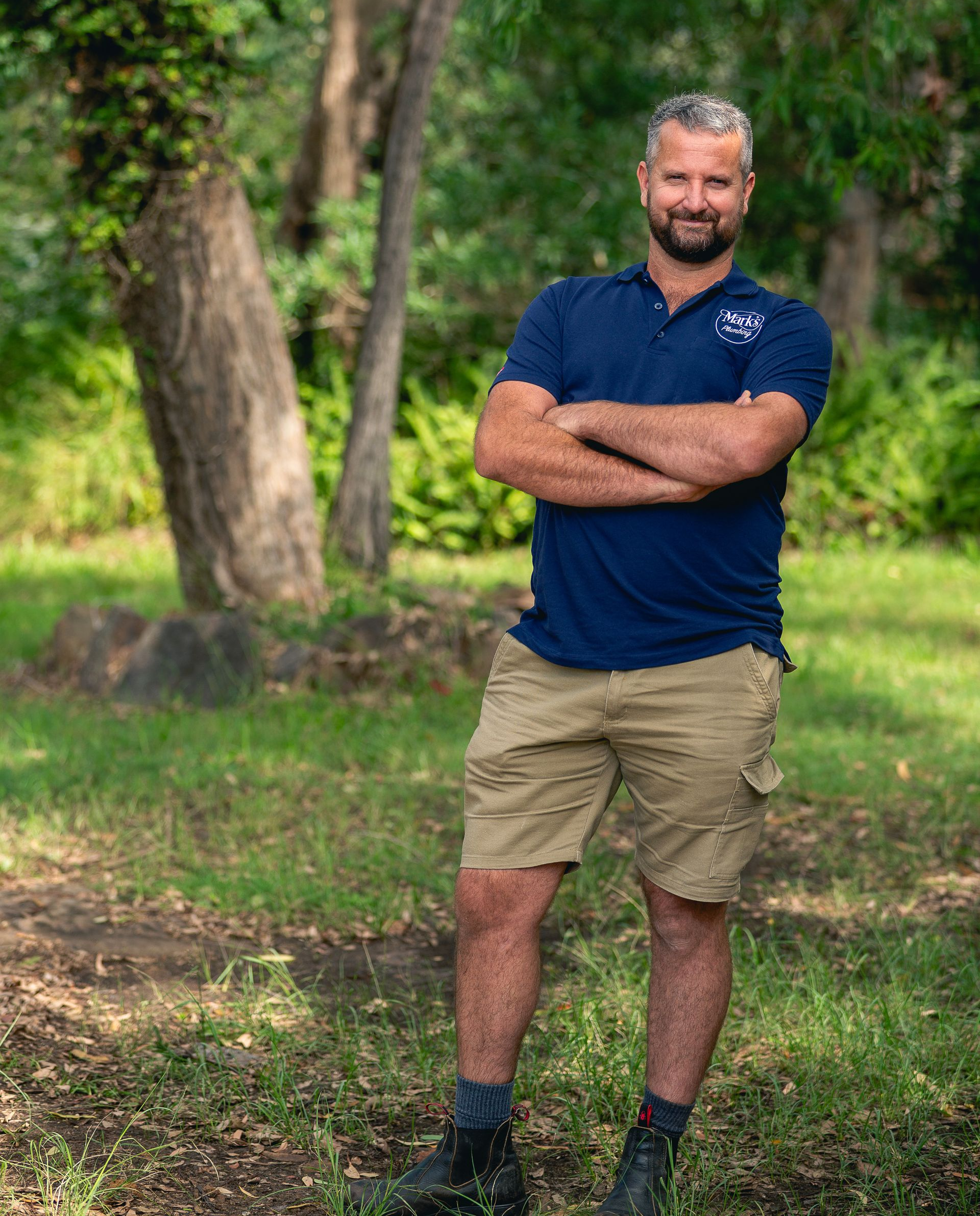 Man Standing Outdoors With Arms Crossed, Wearing a Navy Polo, Khaki Shorts, and Boots — Mark's Plumbing in Noraville, NSW