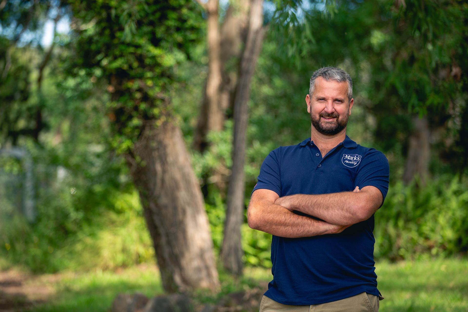 Man in a Navy Shirt Standing Outdoors With Arms Crossed — Mark's Plumbing in Toukley, NSW