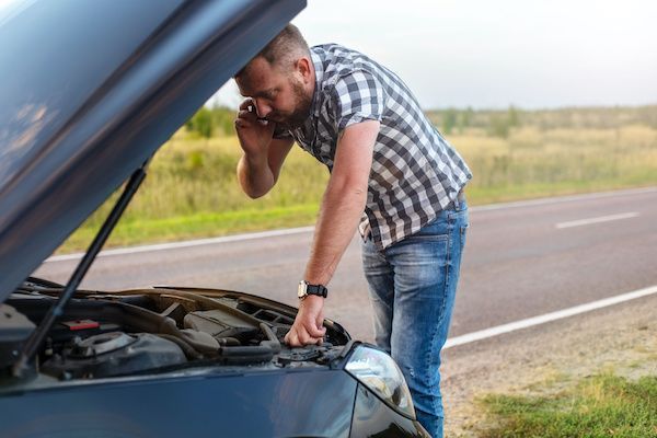 Man leaning over open car hood on roadside, checking engine while holding his head. | Dub's Garage
