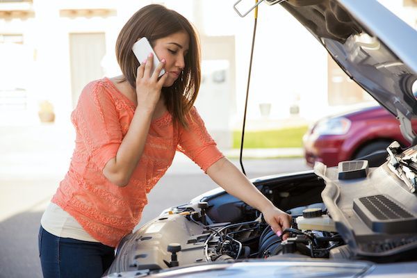 Woman talking on a phone while inspecting a car engine with the hood open, in a driveway. | Dub's Garage