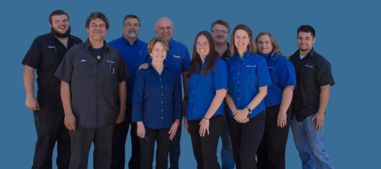 Group of eight people in matching blue shirts standing together against a plain blue background. | Dub's Garage