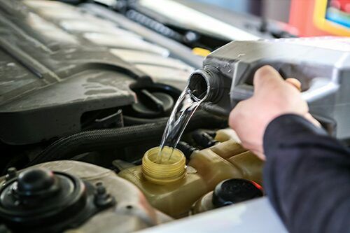Pouring liquid into a car engine reservoir under the hood | Dub's Garage