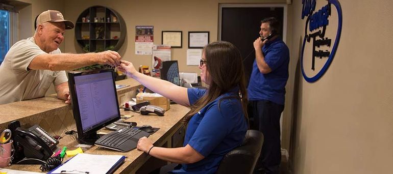 Office scene with three people at a desk, one handing over an item while another stands nearby | Dub's Garage