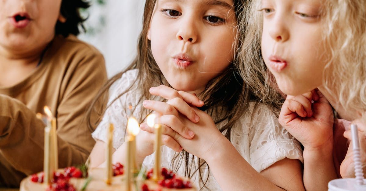 Three children blowing out candles on a cake. The center child is focused, the other two smiling.