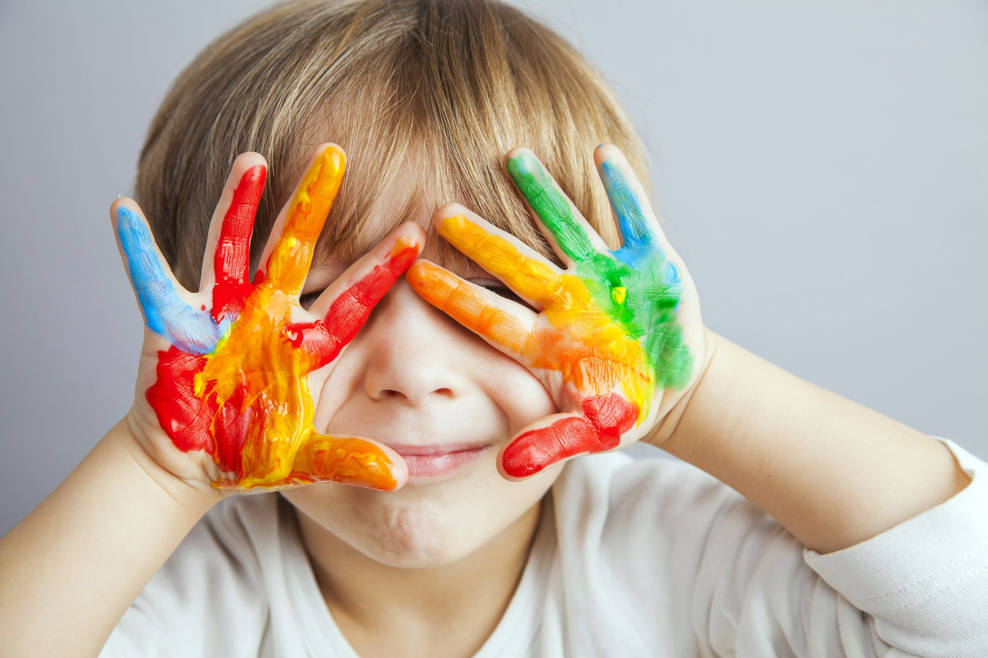 Children huddle together, hands in a circle. Smiling faces, colorful clothes, outside.