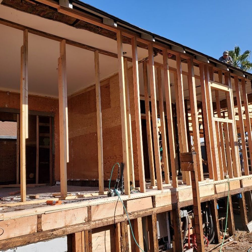 Partially framed wooden house under construction with exposed studs and open porch area