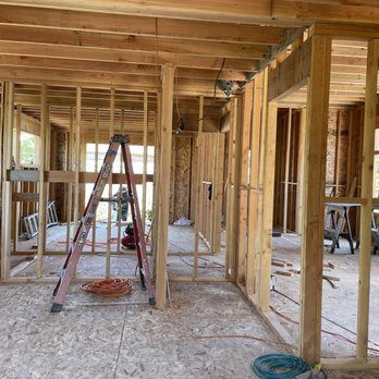 Interior of a wooden house under construction, with exposed framing, ladders, and construction materials.