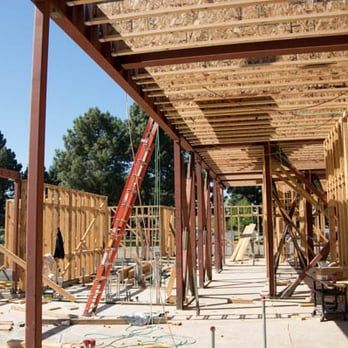 Construction site with wooden framing, red steel posts, and a ladder under a covered roof structure