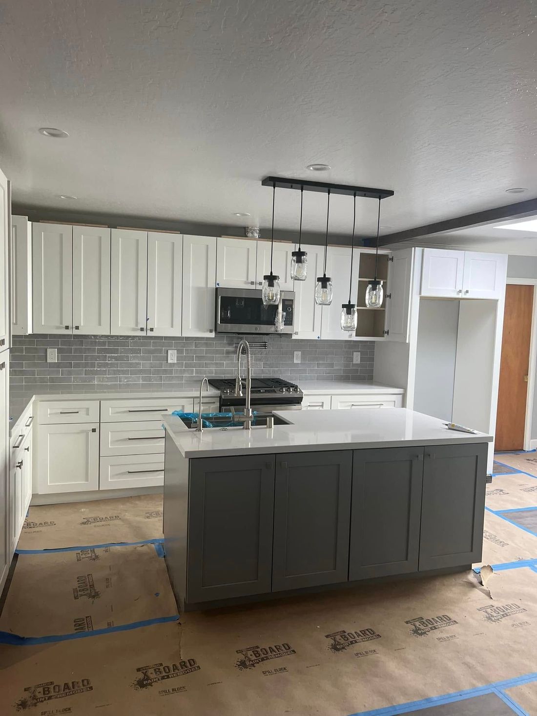 Modern kitchen with white cabinets, gray island, pendant lights, and unfinished flooring.